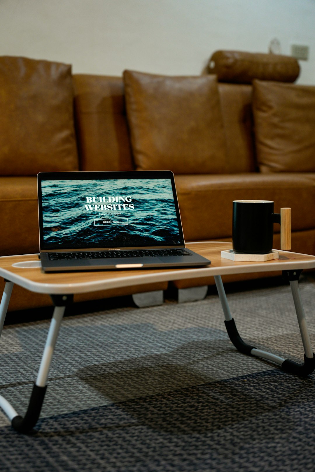 Build websites for your portfolio, resume, internal communications, wedding invitations, and more! A laptop, MacBook, on top of a portable table with coffee tea mug on the side. Portrait.